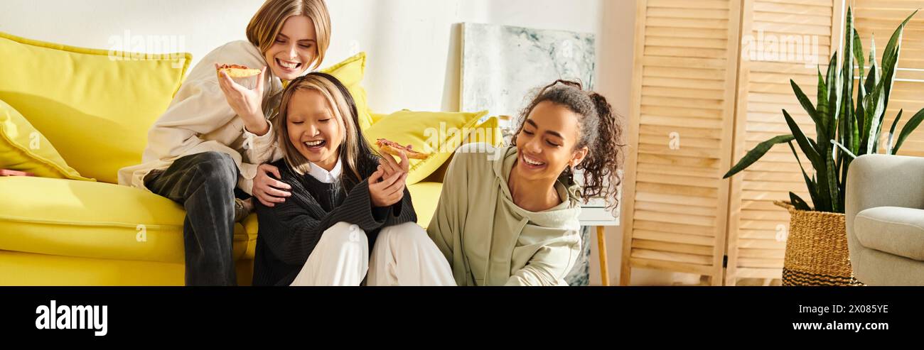 Eine Frau und zwei interrassische Teenager-Mädchen sitzen zusammen auf einer lebhaften gelben Couch und genießen sich gegenseitig Gesellschaft. Stockfoto