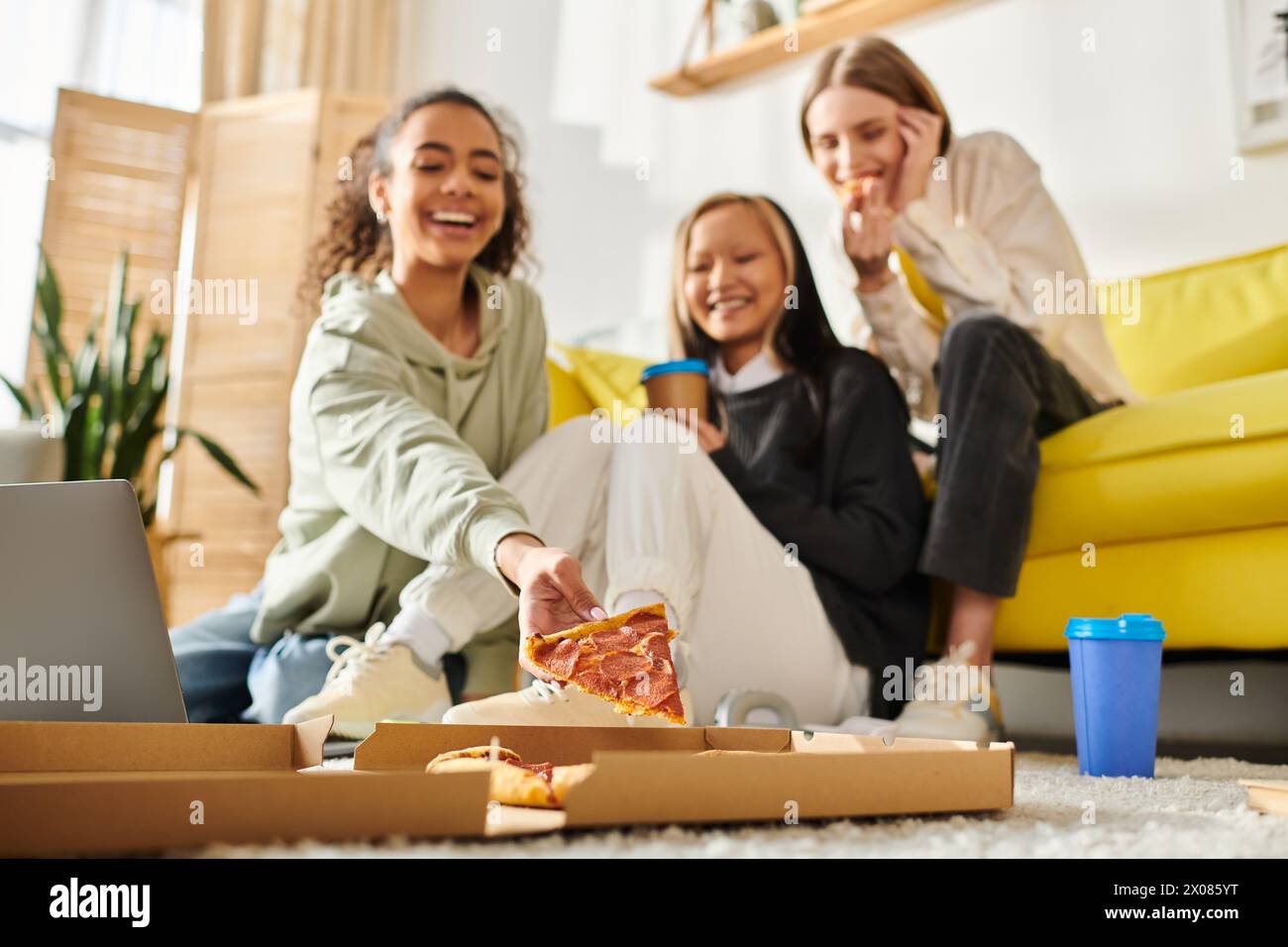 Verschiedene Teenager-Mädchen, die einen zwanglosen Treffpunkt genießen, auf dem Boden sitzen und gemeinsam Pizza-Scheiben genießen. Stockfoto