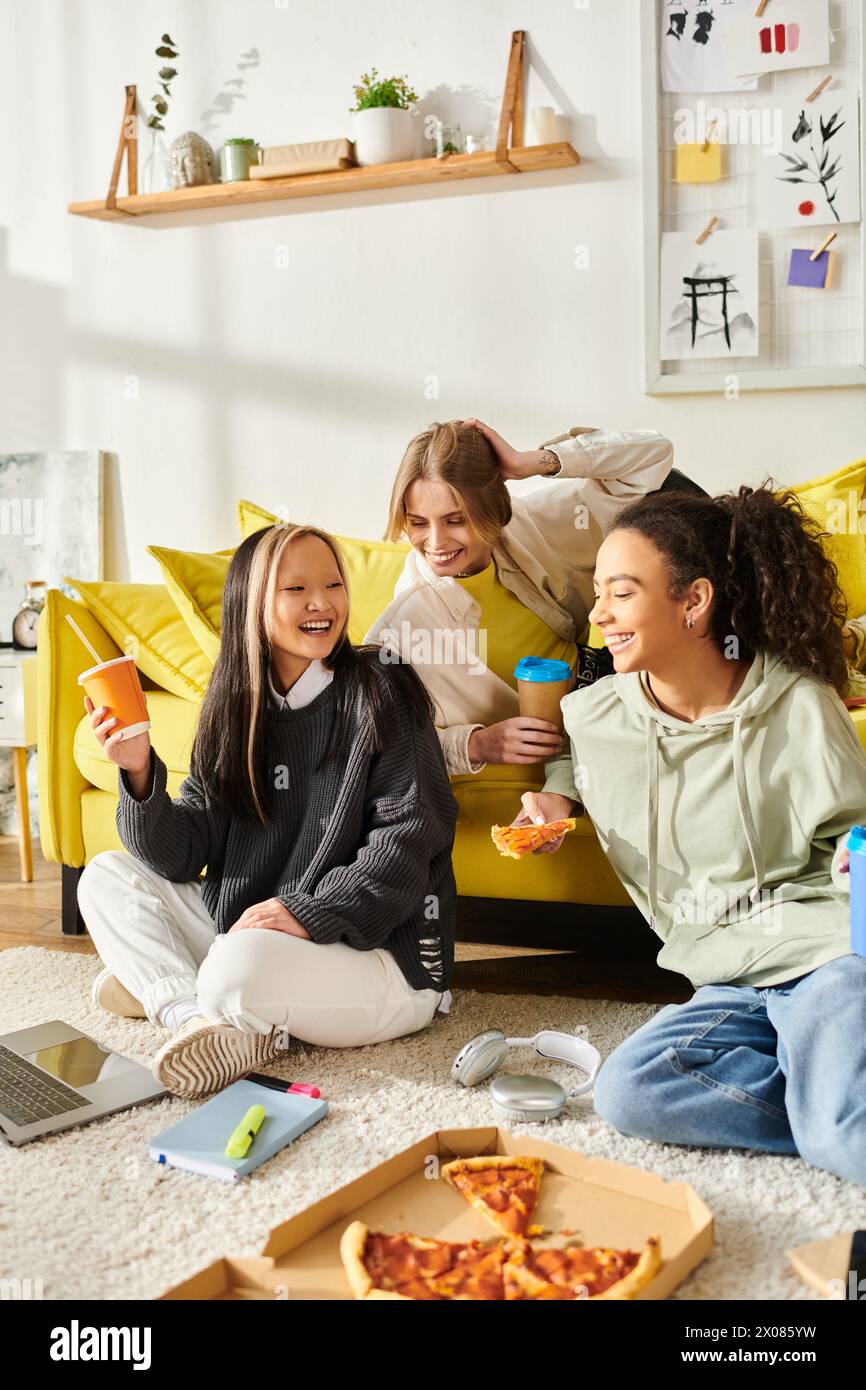 Vielfältige junge Frauen genießen sich auf einer hellgelben Couch in gemütlicher Wohnzimmeratmosphäre. Stockfoto