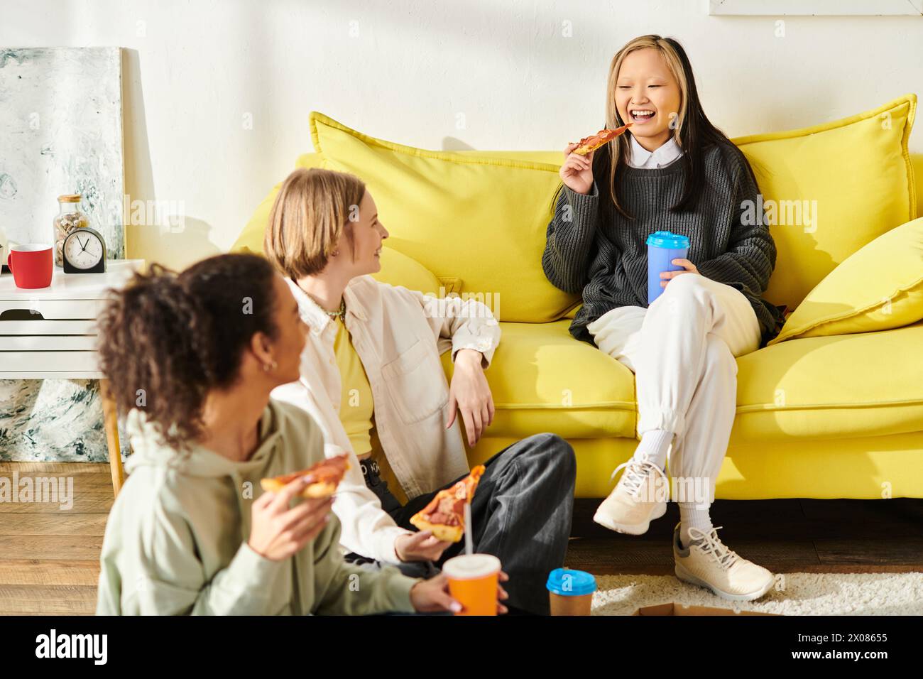 Eine vielfältige Gruppe Teenager-Mädchen, die sich zu Hause auf einer lebhaften gelben Couch amüsieren. Stockfoto