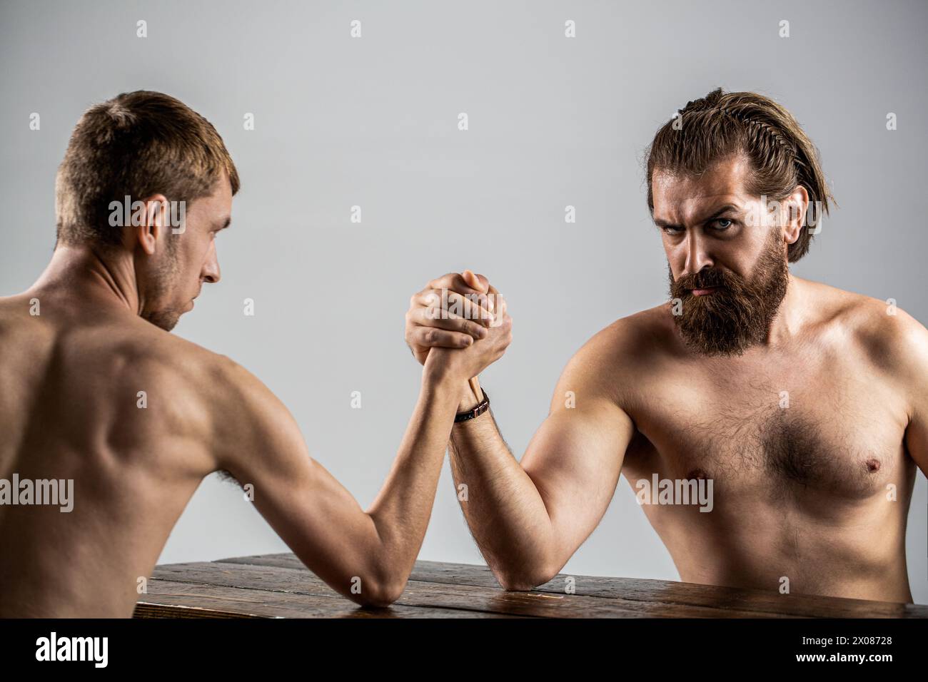 Arme ringen dünne Hand, großer starker Arm im Studio. Zwei Männerhände umklammten Arm Wrestling, stark und schwach, ungleiche Übereinstimmung. Stark muskulös bärtiger Mann Stockfoto