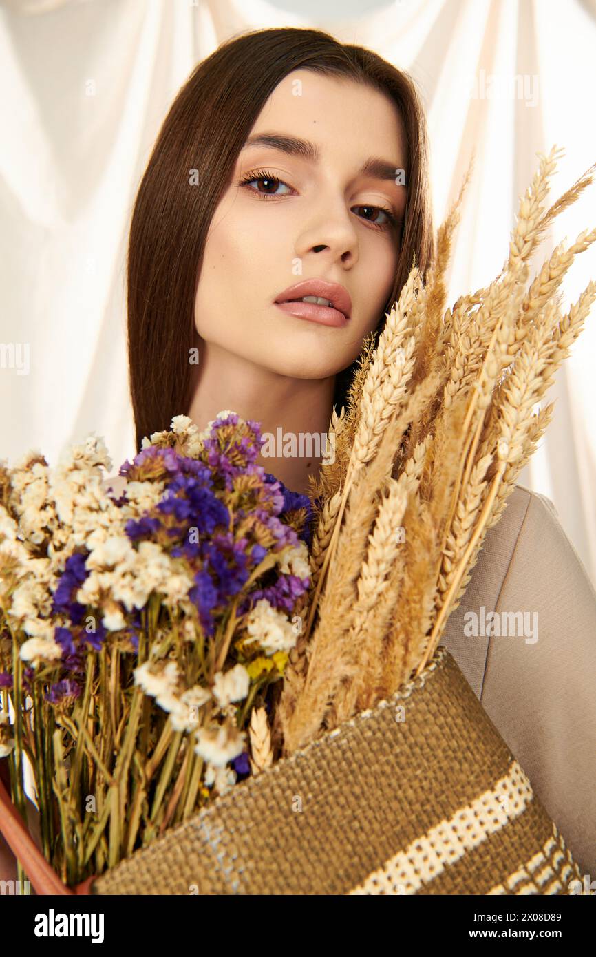 Eine junge Frau mit langen brünetten Haaren verströmt eine Sommerstimmung, während sie in einem Studio einen Strauß getrockneter Blumen hält. Stockfoto