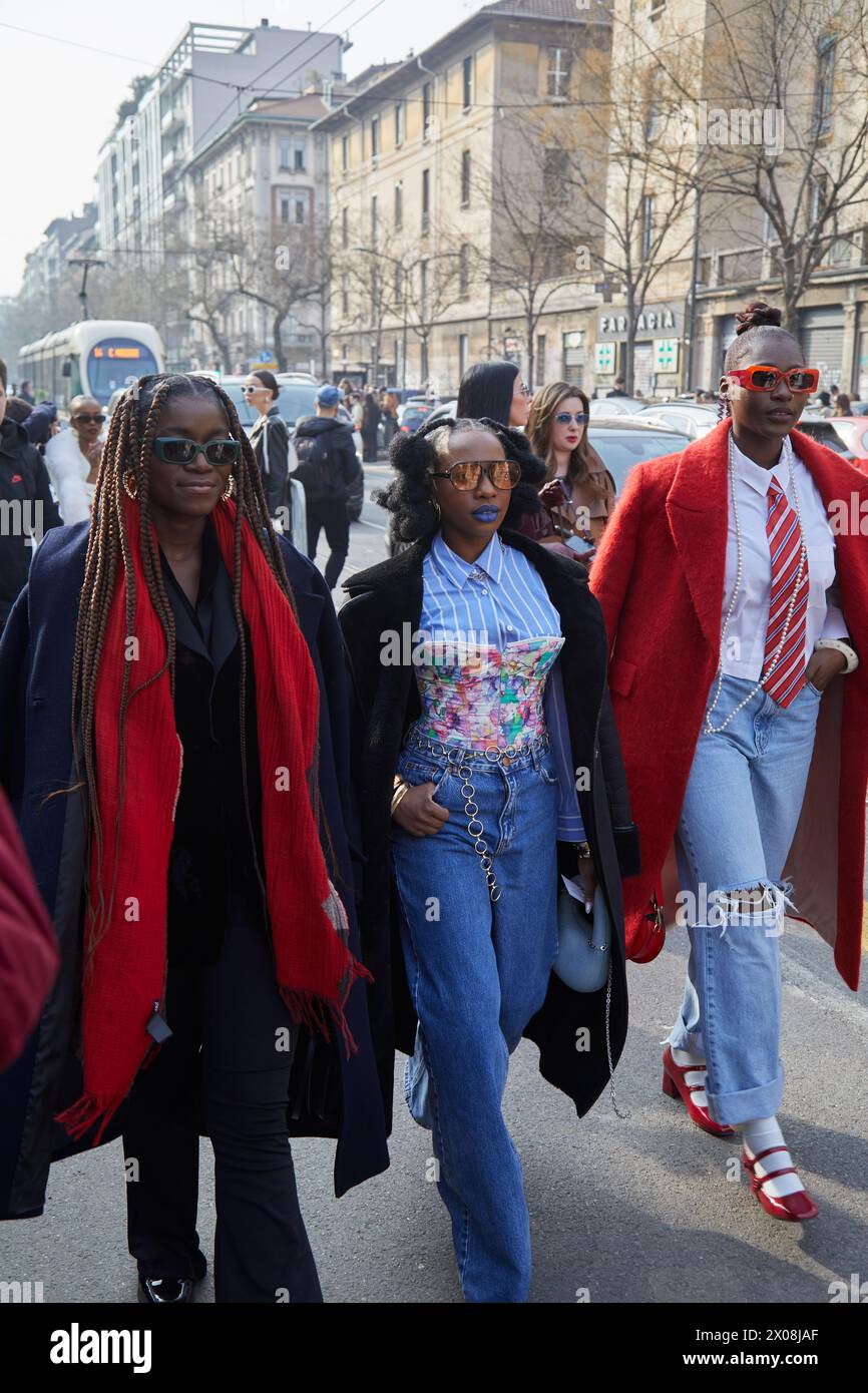MAILAND, ITALIEN - 21. FEBRUAR 2024: Frauen mit schwarzem Mantel, rotem Schal und Jeanshose vor der Fendi Fashion Show, Mailand Fashion Week Street Style Stockfoto