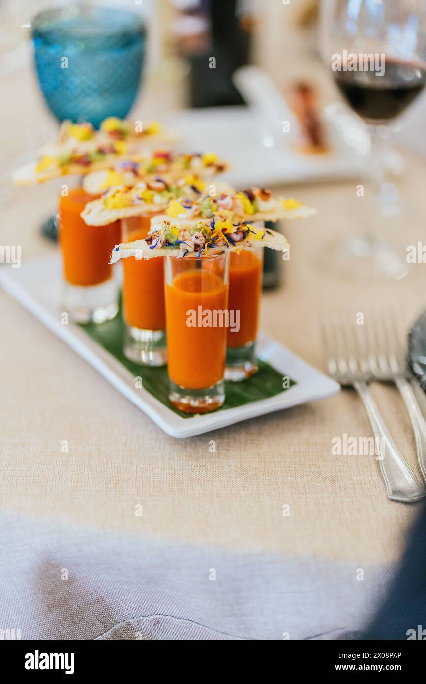 Eine künstlerische Präsentation von Orangensuppen-Shootern mit üppig garnierten Crackern auf einem eleganten Tisch Stockfoto