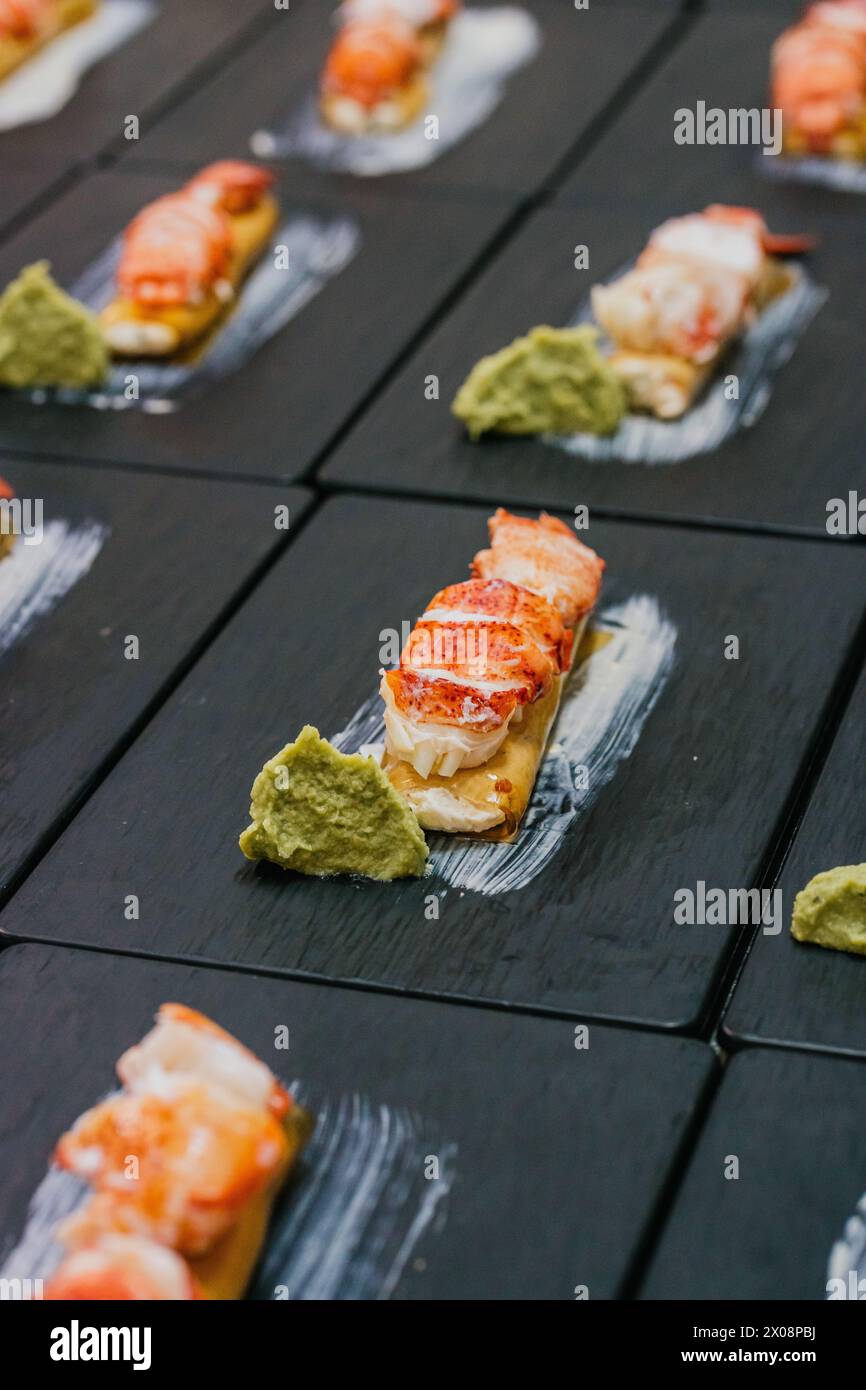 Luxuriöse Hummer-Canapes gepaart mit einem Klecks grüner Soße, sorgfältig auf einem schicken schwarzen Schieferbrett für eine Veranstaltung mit Catering platziert Stockfoto