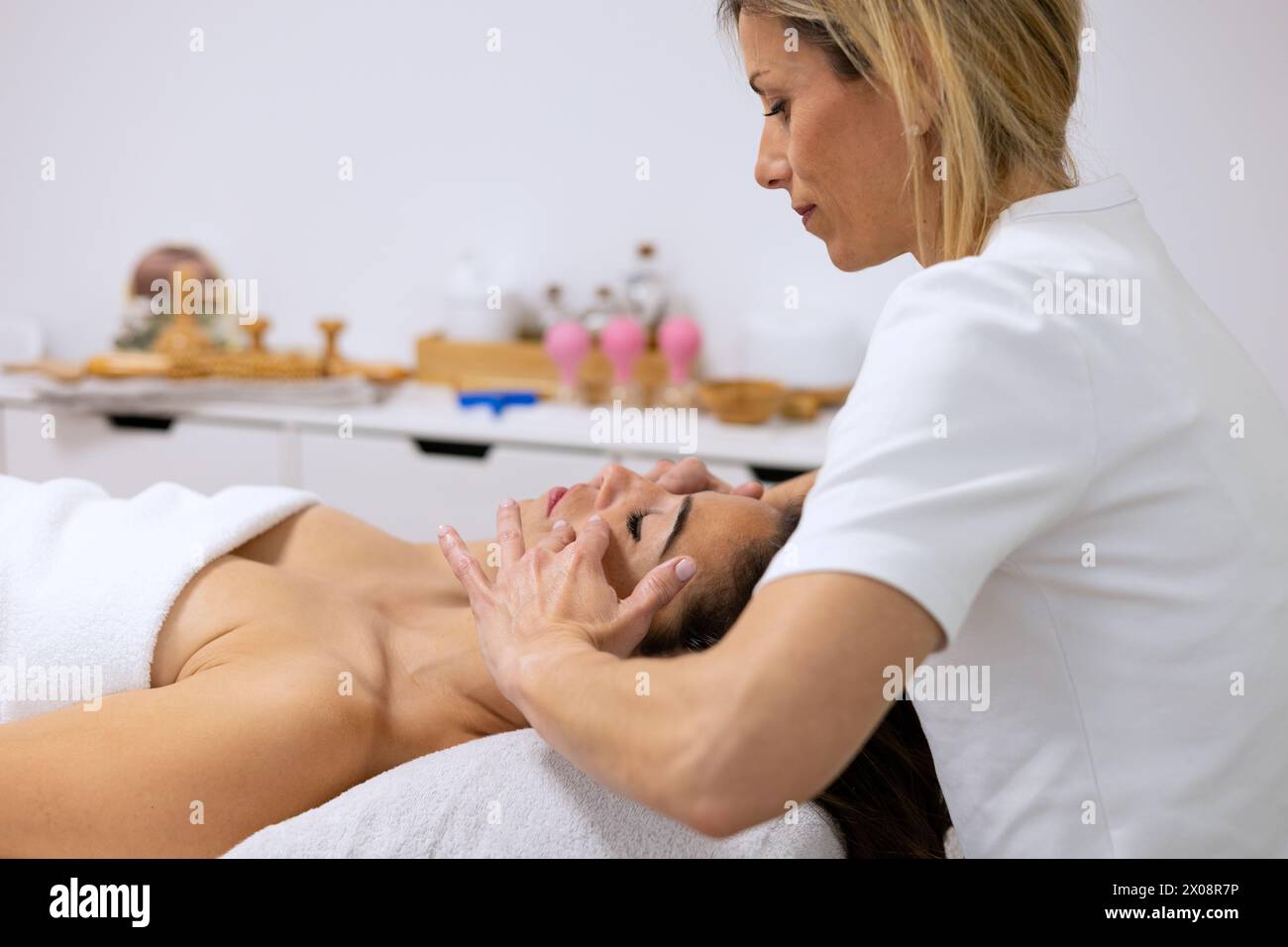 Ein erfahrener Massagetherapeut führt eine sanfte Rückenmassage bei einem entspannten Kunden in einer ruhigen Umgebung durch Stockfoto