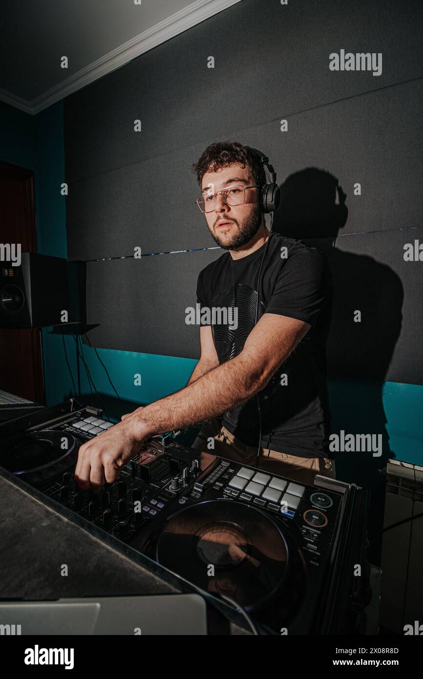Ein fokussierter DJ mit Kopfhörern, der Musik auf seinem Deck in gemütlicher Atmosphäre im Studio mischt, beleuchtet durch sanfte Beleuchtung Stockfoto