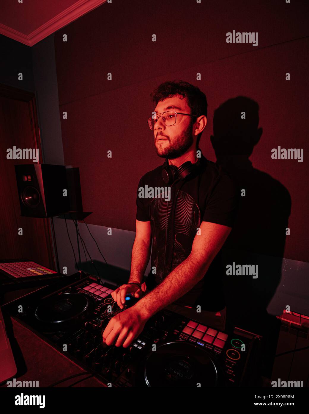 Ein konzentrierter DJ mischt Songs auf einem professionellen DJ-Deck, hervorgehoben durch die rote Beleuchtung, und schafft so eine stimmungsvolle Club-Umgebung Stockfoto