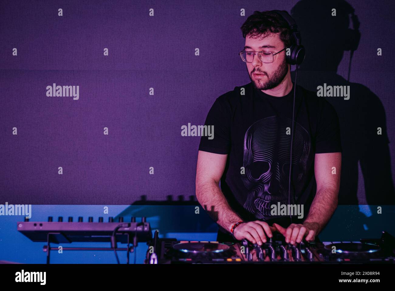 Ein fokussierter DJ mischt auf einer Konsole bei einem lebhaften Clubevent, hervorgehoben durch violette Farbtöne und stimmungsvolle Beleuchtung Stockfoto