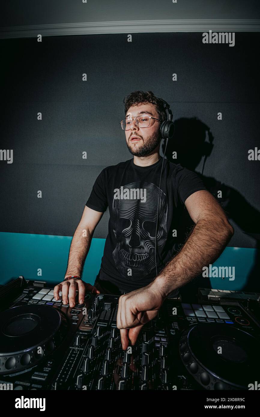 Ein aufmerksamer männlicher DJ in Kopfhörern mischt auf fachmännische Weise Musik auf einem fortschrittlichen DJ-Controller mit stimmungsvoller Beleuchtung Stockfoto
