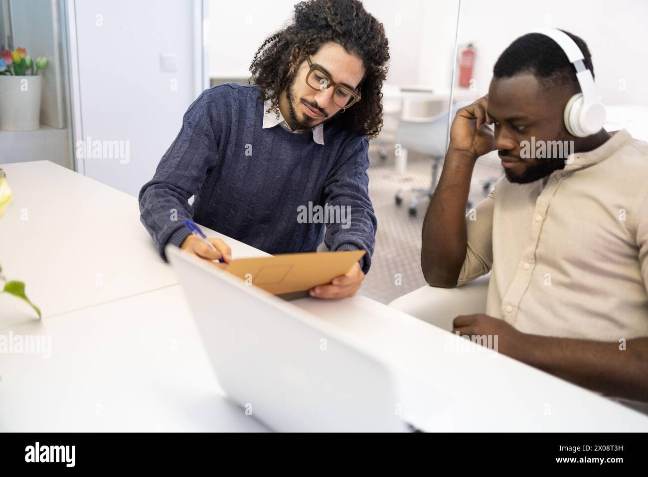 Zwei professionelle Männer in einem Büro, einer aus dem Nahen Osten, der Notizen macht und der andere Afroamerikaner Musik hört. Stockfoto