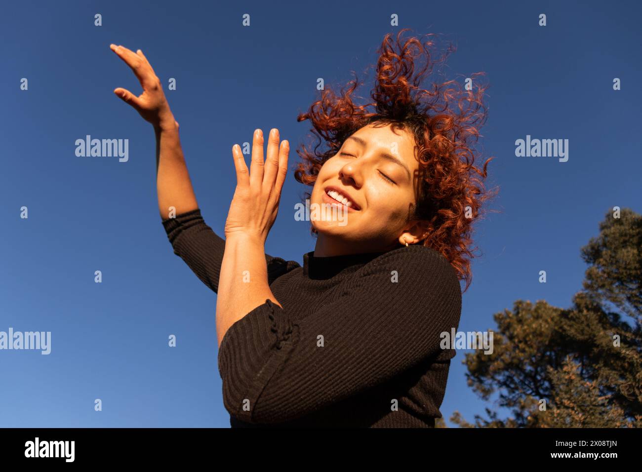 Eine fröhliche zeitgenössische Tänzerin bewegt sich anmutig unter einem klaren blauen Himmel, ihre roten Locken hüpfen im Sonnenlicht Stockfoto