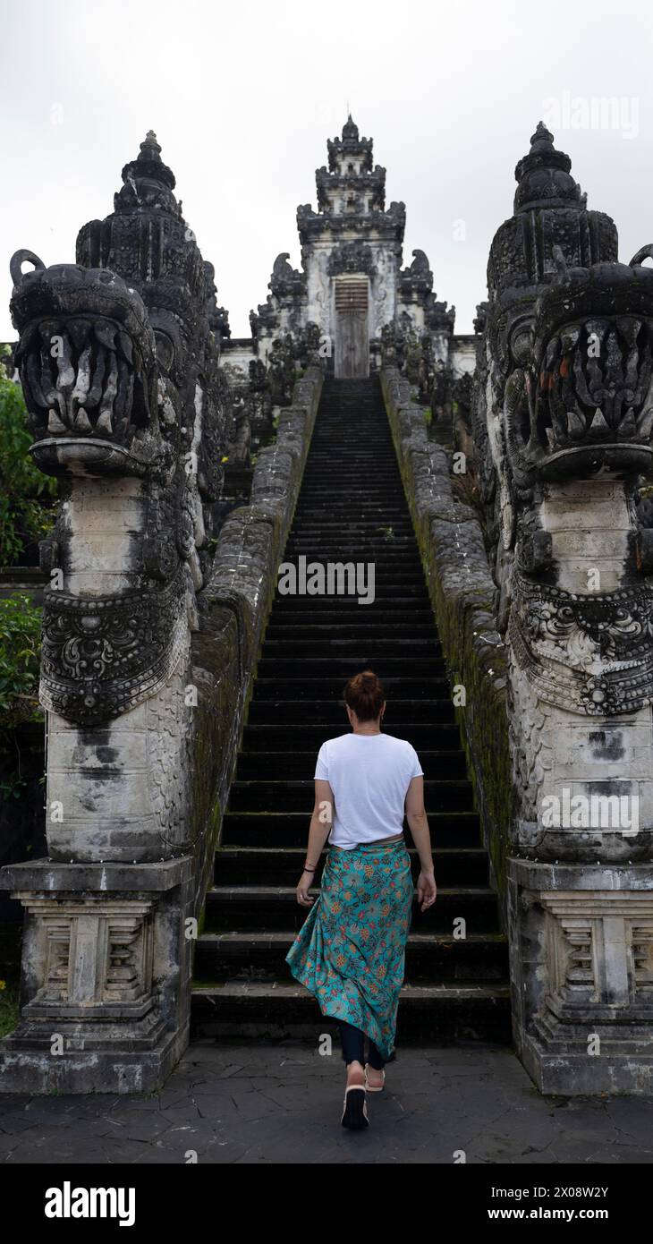 Rückansicht der nicht erkennbaren weiblichen Reisenden steigt die antike Treppe von Pura Penataran Agung Lempuyang, einem berühmten balinesischen Tempel, hinauf Stockfoto