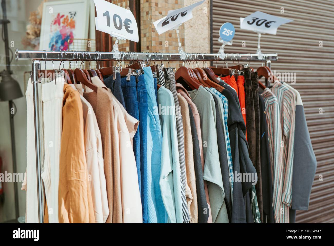 Kleidungsstücke mit Preisschildern, die auf großartige Angebote hinweisen, hängen in einem Boutique-Geschäft an der Schiene und laden so preisbewusste Modeliebhaber ein Stockfoto