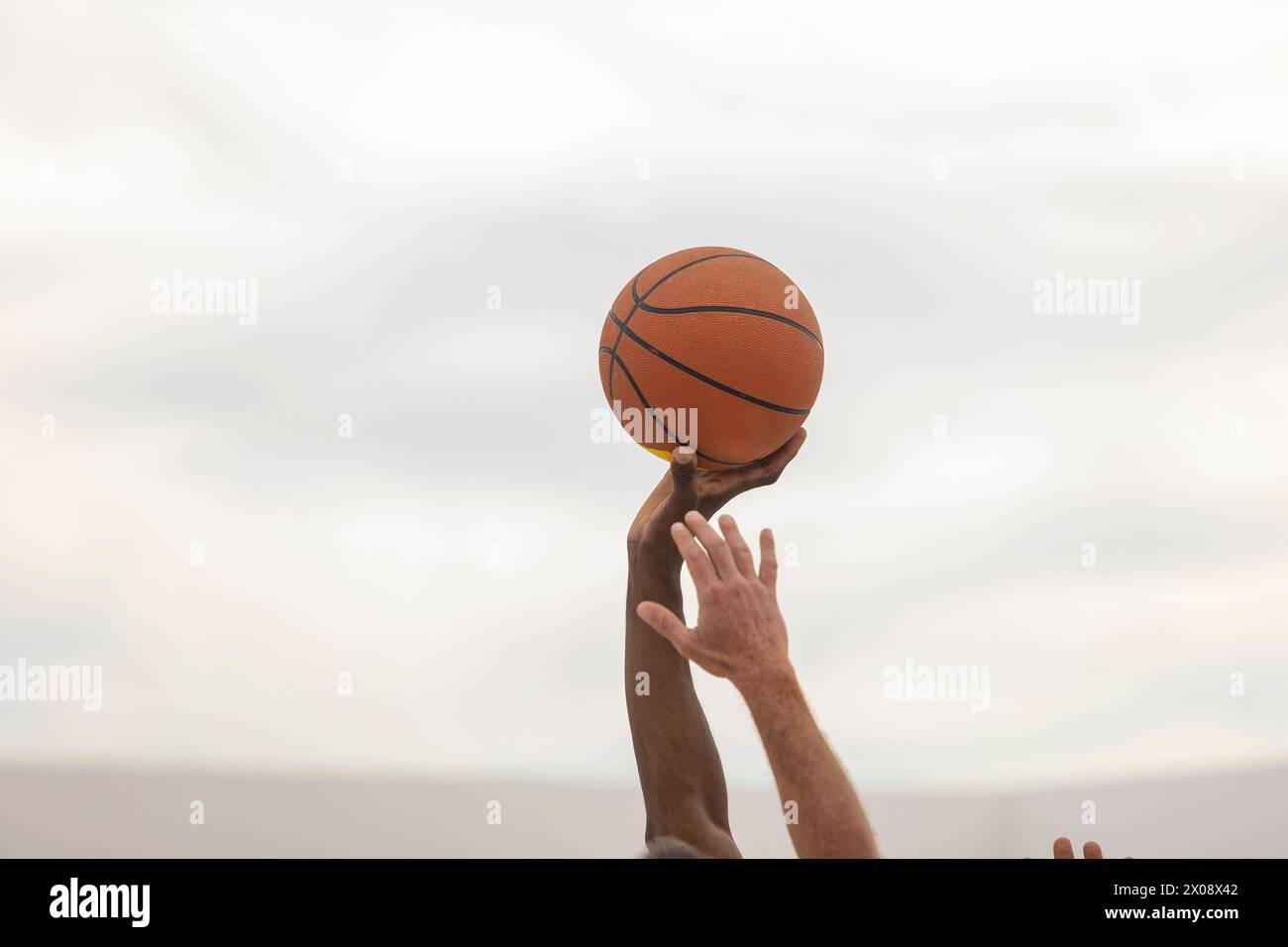 Ein Basketball, der in der Hand eines Spielers vor einem weichen Hintergrund gehalten wird, bereit für Action auf dem Platz im Freien Stockfoto