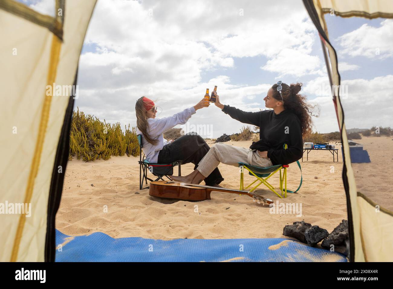 Ein paar tosten mit Flaschen Bier und feiern ihre Zuneigung, während sie vor ihrem Zelt auf einem malerischen Strandcamping sitzen Stockfoto