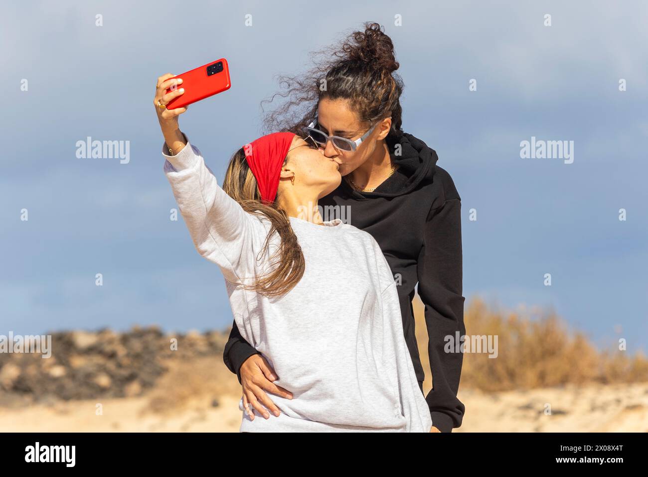 Ein glückliches Paar fängt einen zärtlichen Moment mit einem Selfie-Kuss während ihres Strandcampings unter einem bewölkten Himmel ein Stockfoto