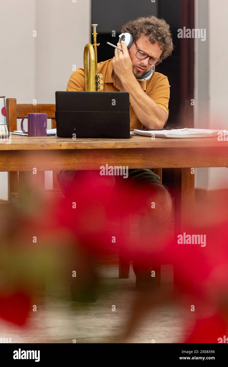 Ein einarmiger männlicher Trompeter arbeitet an seinem kreativen Prozess, liest Notizen und übt mit seiner Trompete in der entspannten Umgebung seines Zuhauses Stockfoto