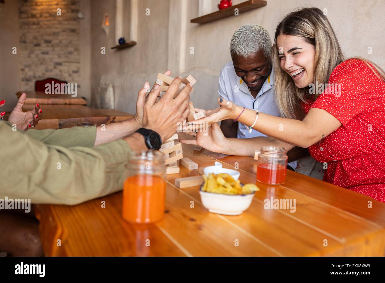 Eine lebhafte Gruppe von Freunden, die ein Spiel Jenga an einem Holztisch in einer zwanglosen Bar mit fröhlichem Ausdruck genießen Stockfoto