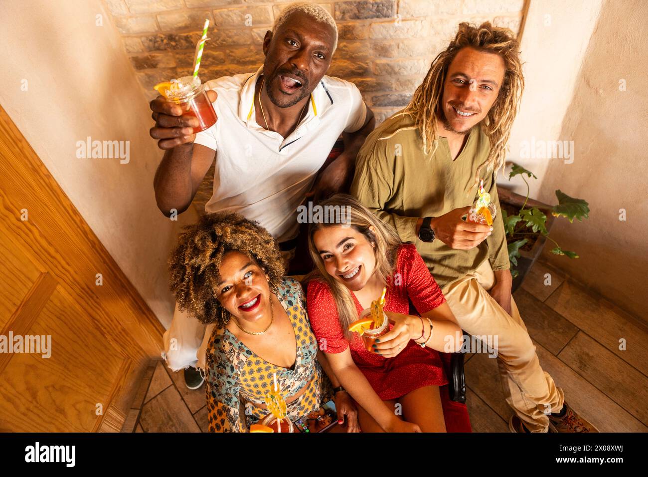 In einer Bar versammelt sich eine Gruppe lächelnder Freunde, die bei Cocktails anstoßen und eine fröhliche und entspannte Atmosphäre schaffen Stockfoto