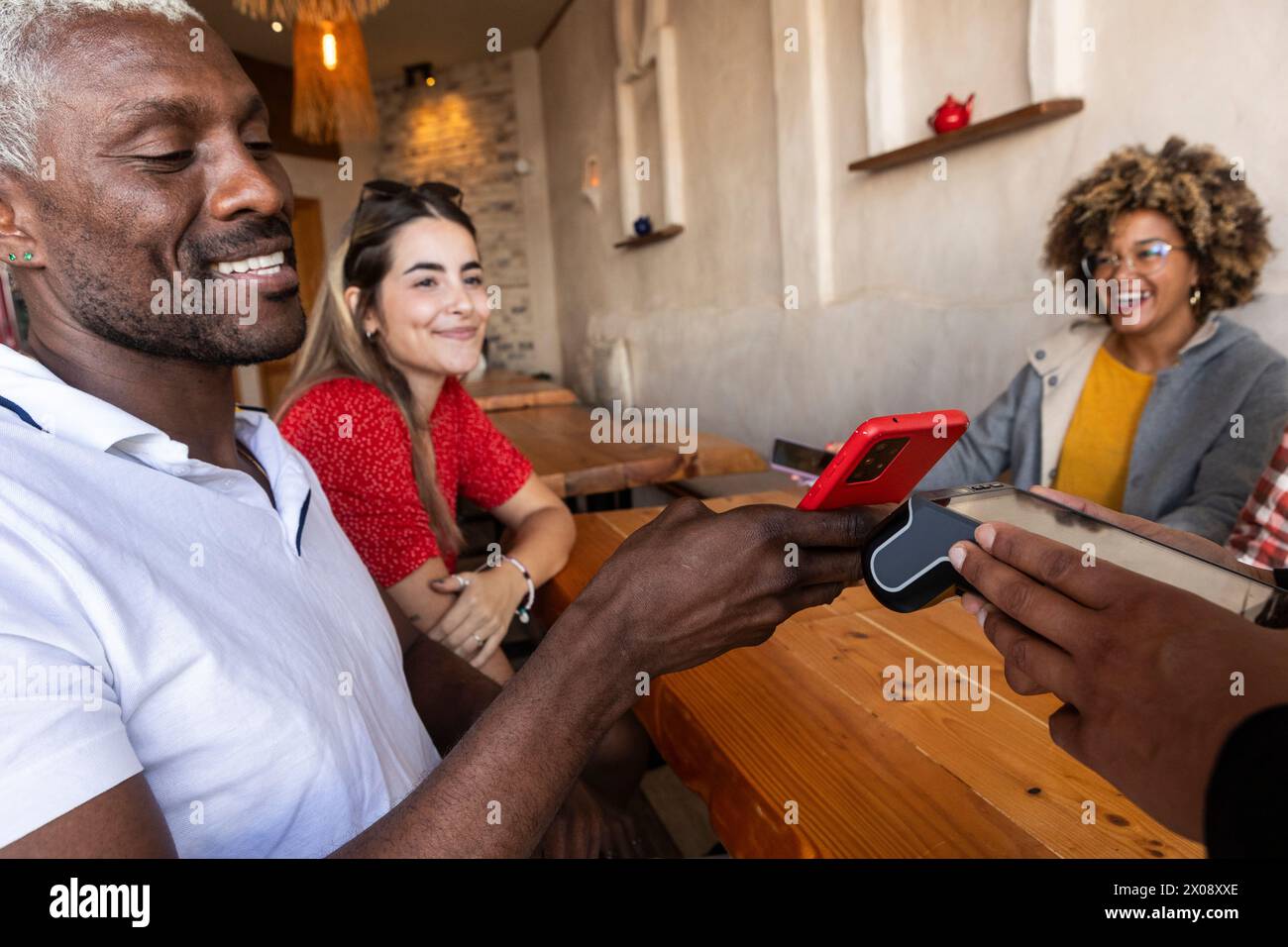Eine vielfältige Gruppe von Freunden genießt eine gute Zeit zusammen, lacht und interagiert mit einem Smartphone in einer rustikalen Bar Stockfoto