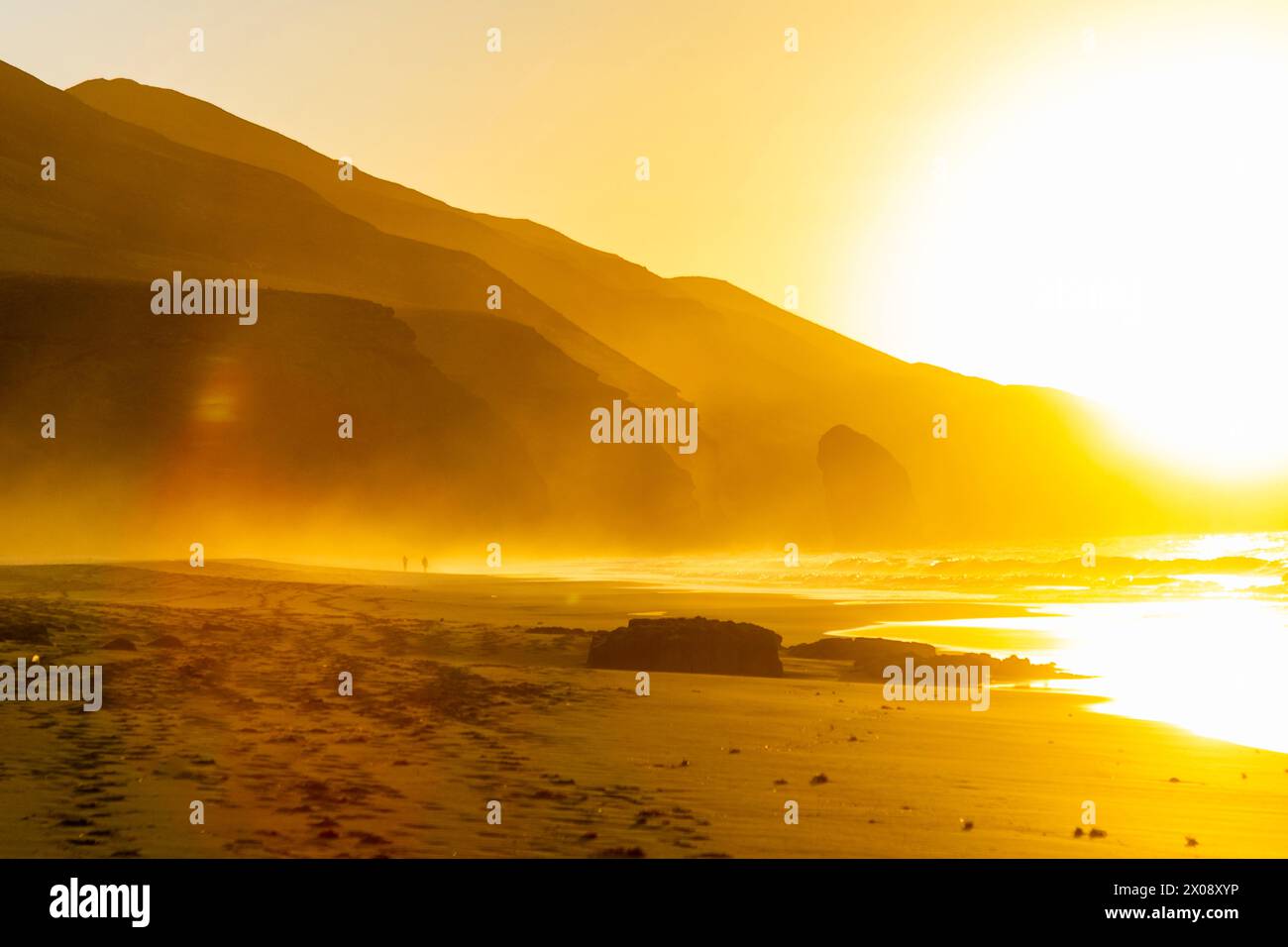 Ein ruhiger Sonnenuntergang taucht den Süden von Fuerteventura am Strand Cofete in ein goldenes Licht, mit Silhouetten von Menschen und Bergen in der Ferne Stockfoto