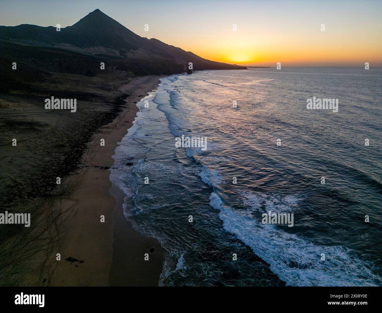 Ein Luftbild fängt die ruhige Schönheit des Strandes Cofete ein, der während des Sonnenuntergangs vor den zerklüfteten Bergen der Südküste von Fuerteventura liegt Stockfoto