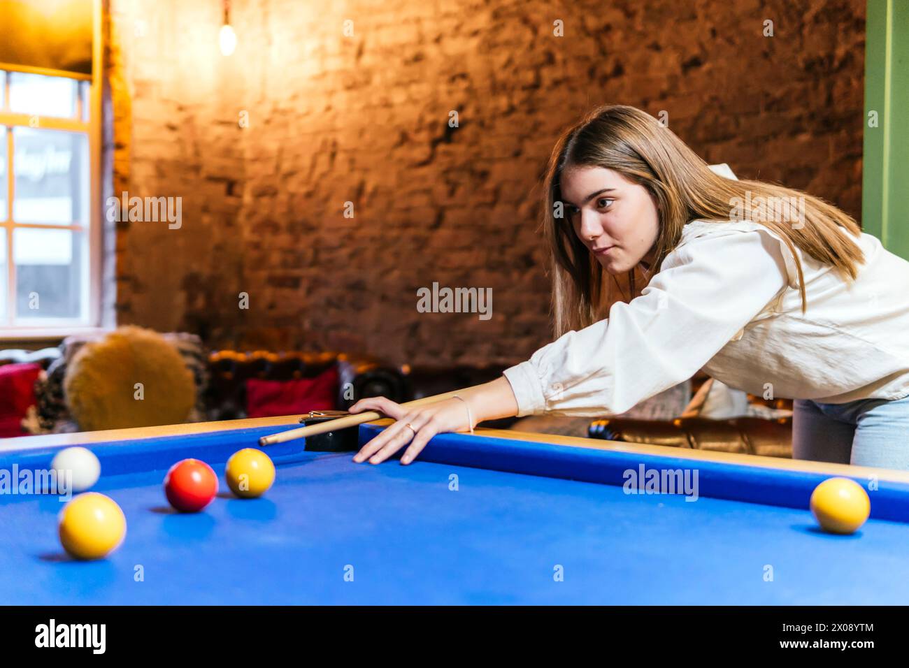 Eine junge Frau zielt auf einen blauen Billardtisch während eines zwanglosen Billardspiels mit Freunden in einer gemütlichen Innenumgebung Stockfoto