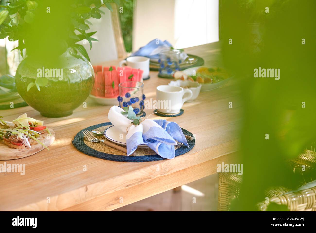 Durch ein üppiges Laub wird ein ruhiger Frühstückstisch auf der Terrasse erblickt, der einen ruhigen Start in den Tag verspricht Stockfoto