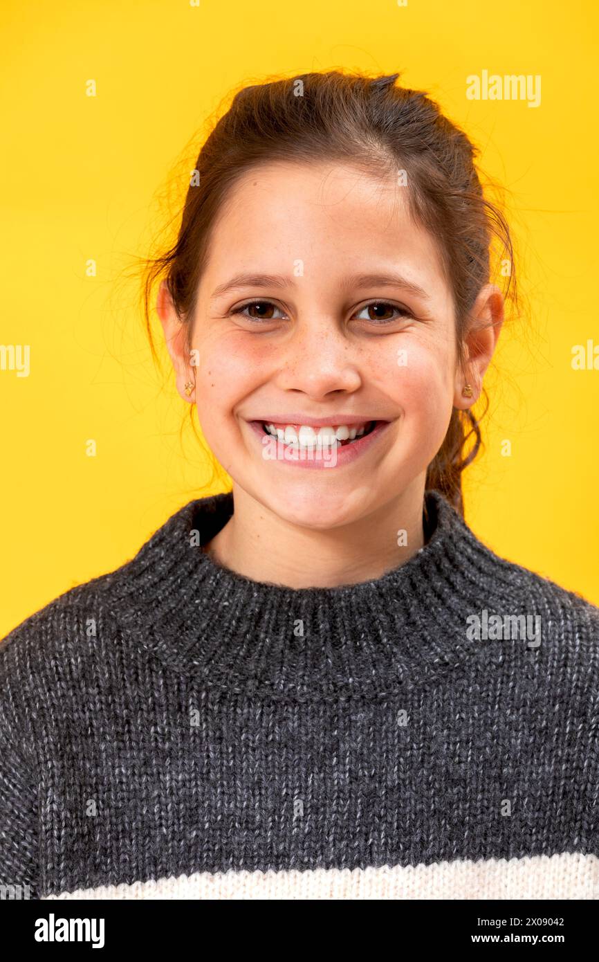 Porträt eines glücklichen jungen Mädchens mit einem hellen Lächeln in einem gemütlichen Pullover vor einem leuchtend gelben Hintergrund Stockfoto