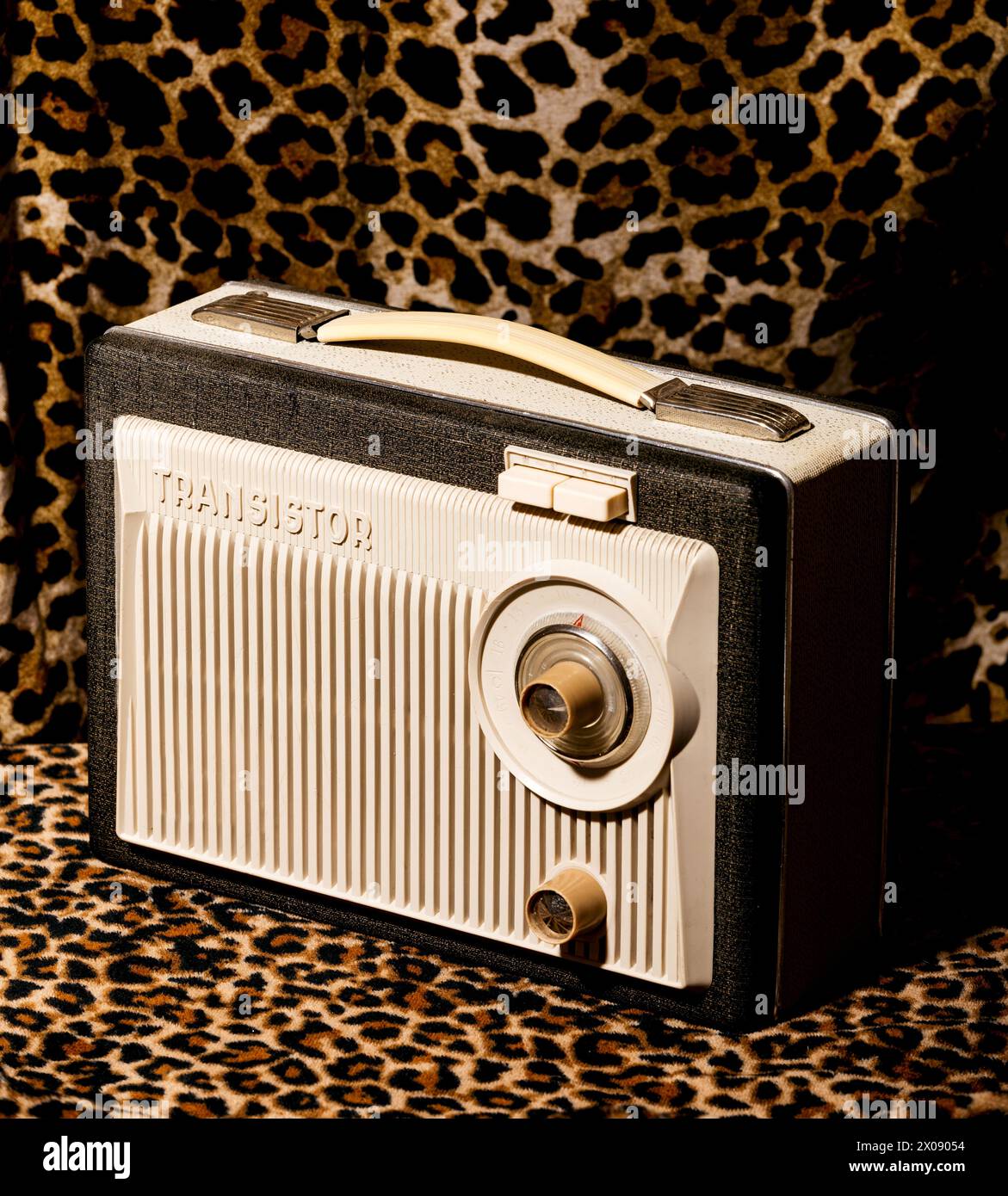 Ein Transistorradio im Retro-Stil mit klassischem Design hebt sich von einem auffälligen Stoff mit Leopardenmuster ab und erinnert an eine nostalgische Ästhetik aus der Mitte des 20. Jahrhunderts. Stockfoto
