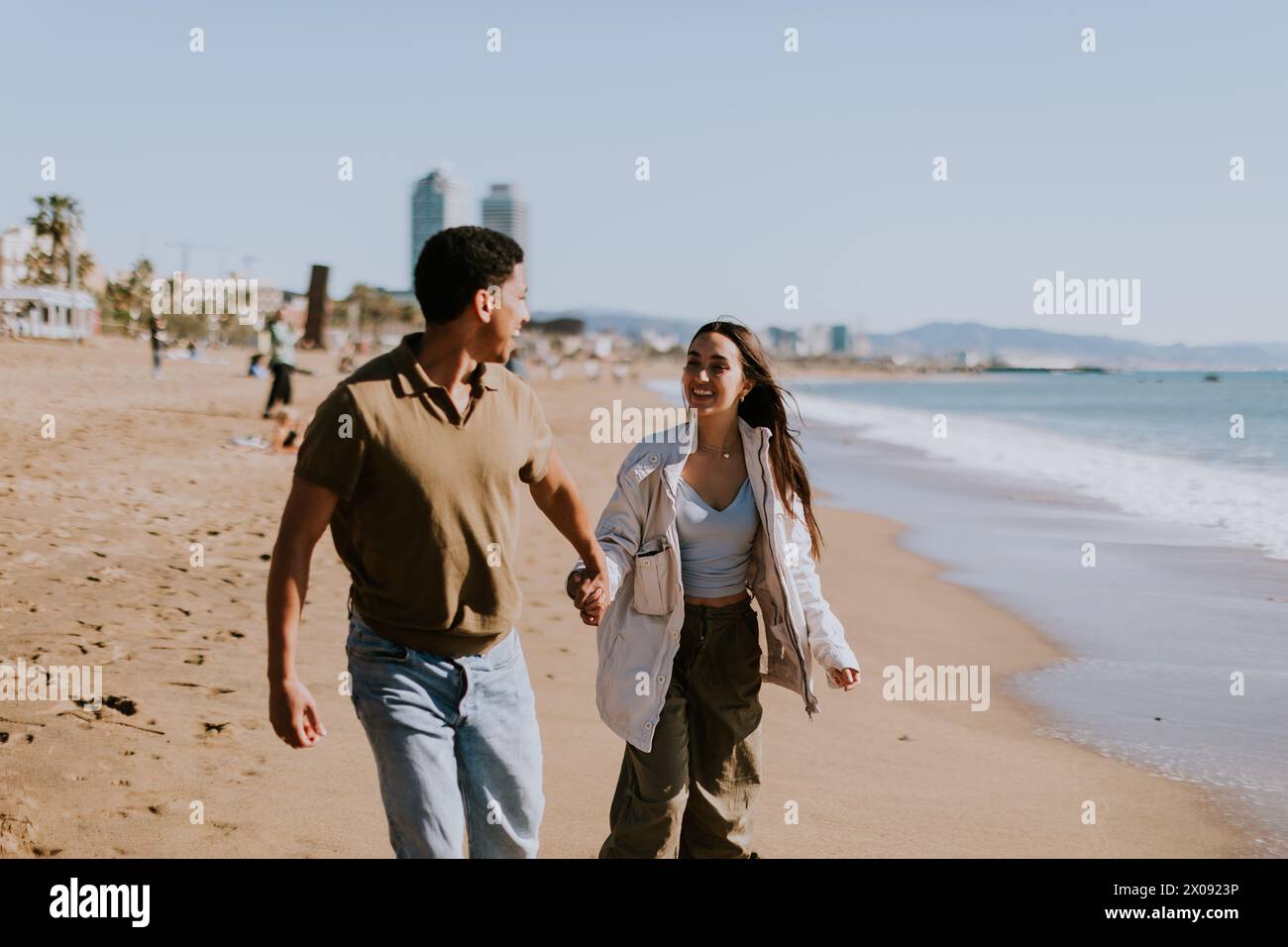 Ein lächelndes Paar genießt einen sorglosen Lauf an einem Sandstrand, Wellen brechen sanft in den Hintergrund Stockfoto