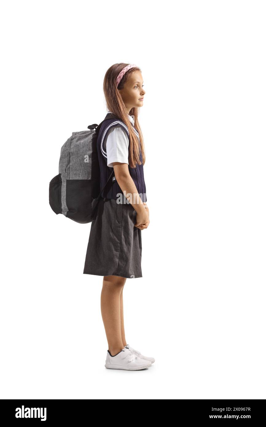 Profilaufnahme eines Schulmädchens in Uniform, das mit einem Rucksack auf Schultern auf weißem Hintergrund steht Stockfoto