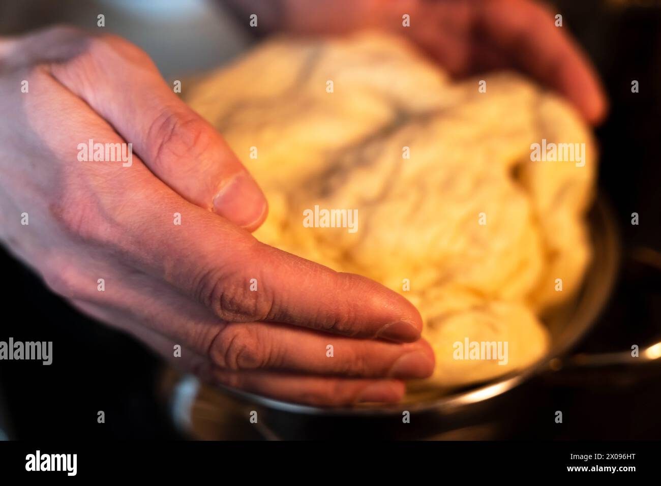 Professioneller Bäcker, der mit Leidenschaft Teig in einer Restaurantküche kntet, mit Nahaufnahme und unscharfen Bewegungen, um die dynamische Bewegung und Erfahrung festzuhalten Stockfoto