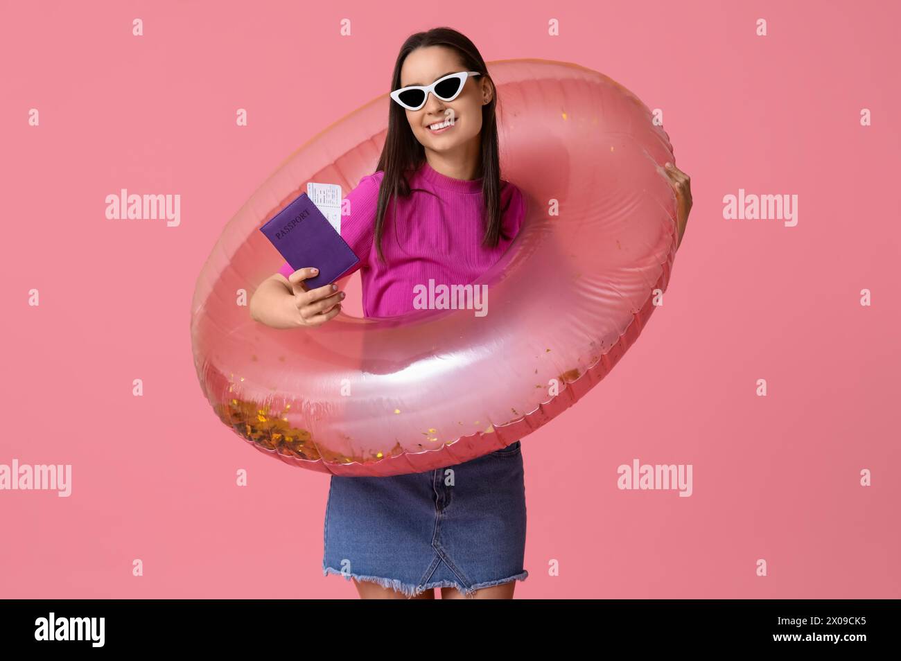 Junge glückliche Frau in Sonnenbrille und aufblasbarem Ring mit Pass auf rosa Hintergrund. Reisekonzept Stockfoto