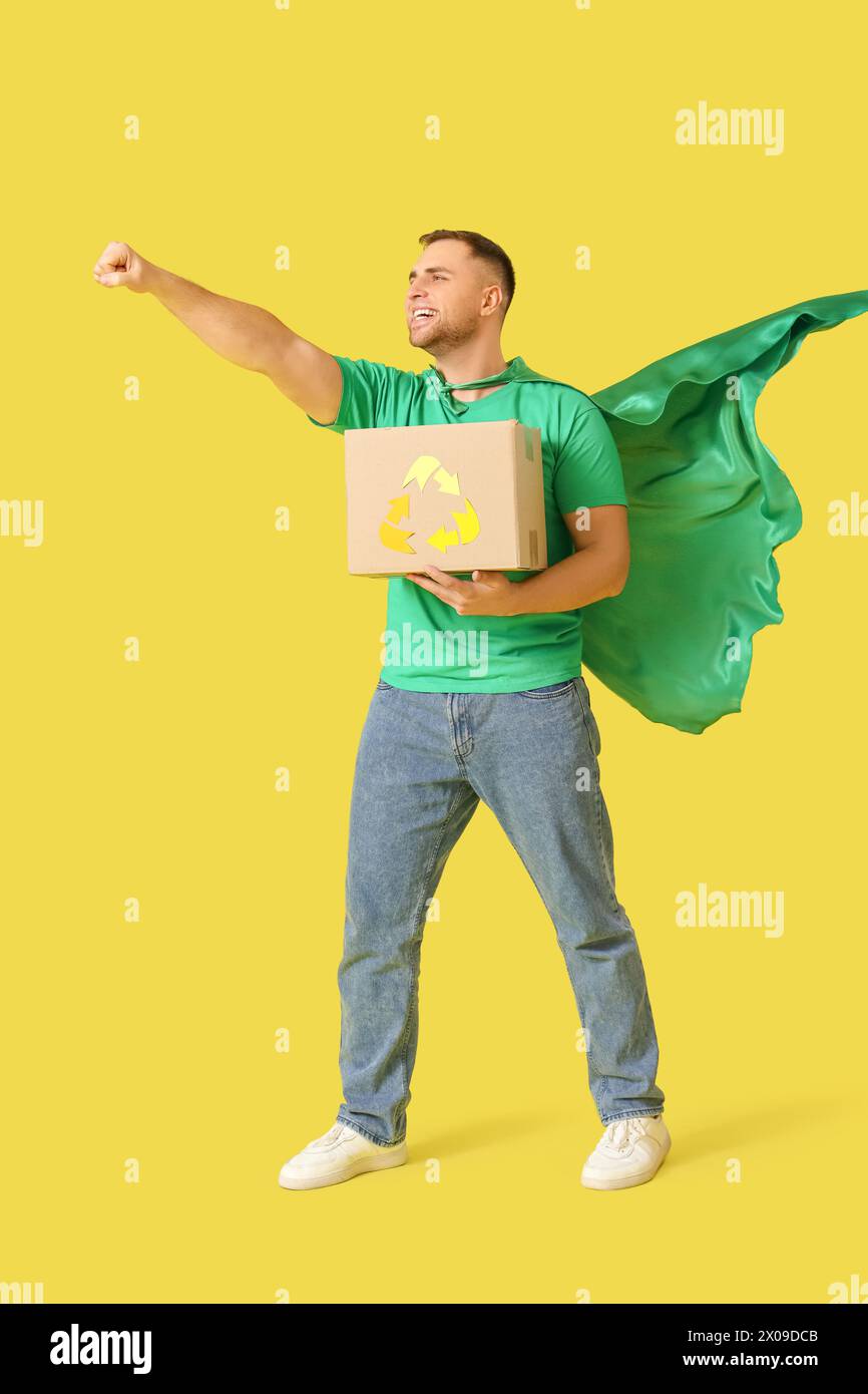 Männlicher Freiwilliger im superheldenumhang mit Recyclingbox auf gelbem Hintergrund Stockfoto