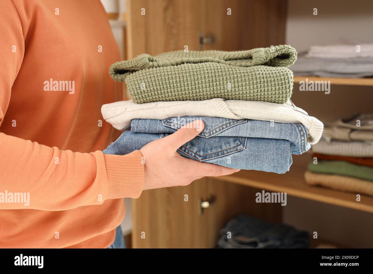 Junger Mann, der zu Hause einen Stapel Kleider in den Schrank legt, Nahaufnahme Stockfoto