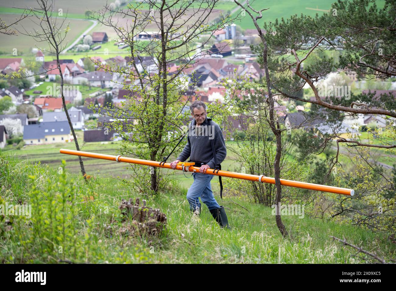 Altenstein, Deutschland. April 2024. Der Geologe Markus Tarasconi untersucht einen Aussichtspunkt bei Altenstein mittels elektromagnetischer Induktion; im Hintergrund ist das Dorf Junkersdorf zu sehen. Ziel der geophysikalischen Vermessung ist es, archäologische Merkmale wie ehemalige Steinmauern oder verbrannte Gebiete ans Licht zu bringen, ohne in den Boden graben zu müssen. Die Ergebnisse können dazu beitragen, die Notwendigkeit und den Nutzen weiterer archäologischer Untersuchungen besser einzuschätzen. Unterhalb der Ruine der Burg Altenstein wird ein Hinrichtungsort und ein Galgen vermutet. Quelle: Pia Bayer/dpa/Alamy Live News Stockfoto
