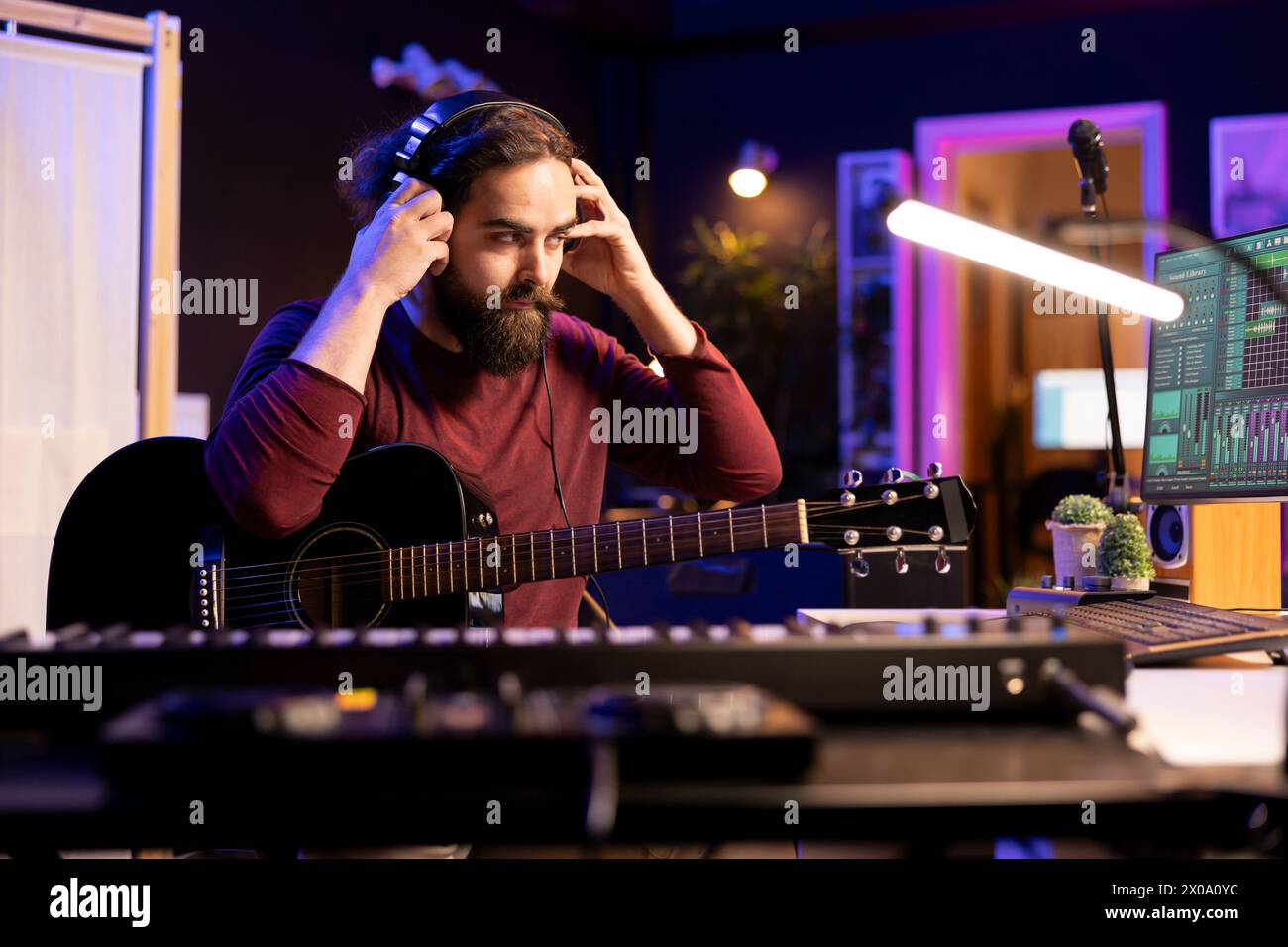 Sound-Komponist, der mit elektronischer Einrichtung im Heimstudio arbeitet und akustische Gitarrenmelodien aufnimmt und abspielt. Musiker, der mit Signalverarbeitungstechniken und Audiosteckern am Schreibtisch arbeitet. Stockfoto