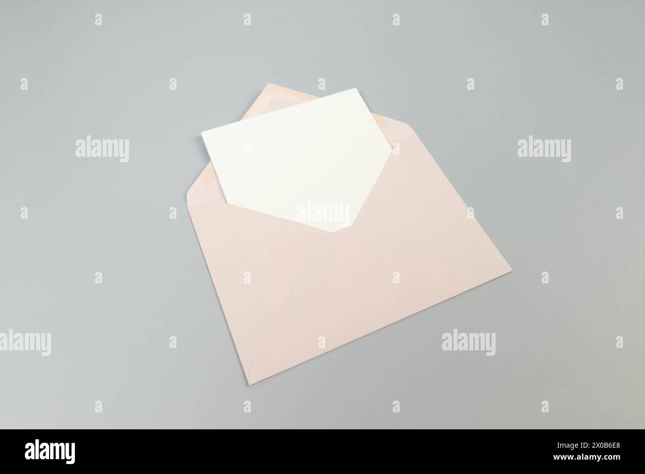 Draufsicht des rosafarbenen Umschlags, weiße Karte auf grauem Hintergrund. Pfosten Sie flach. Kopierbereich. Stockfoto