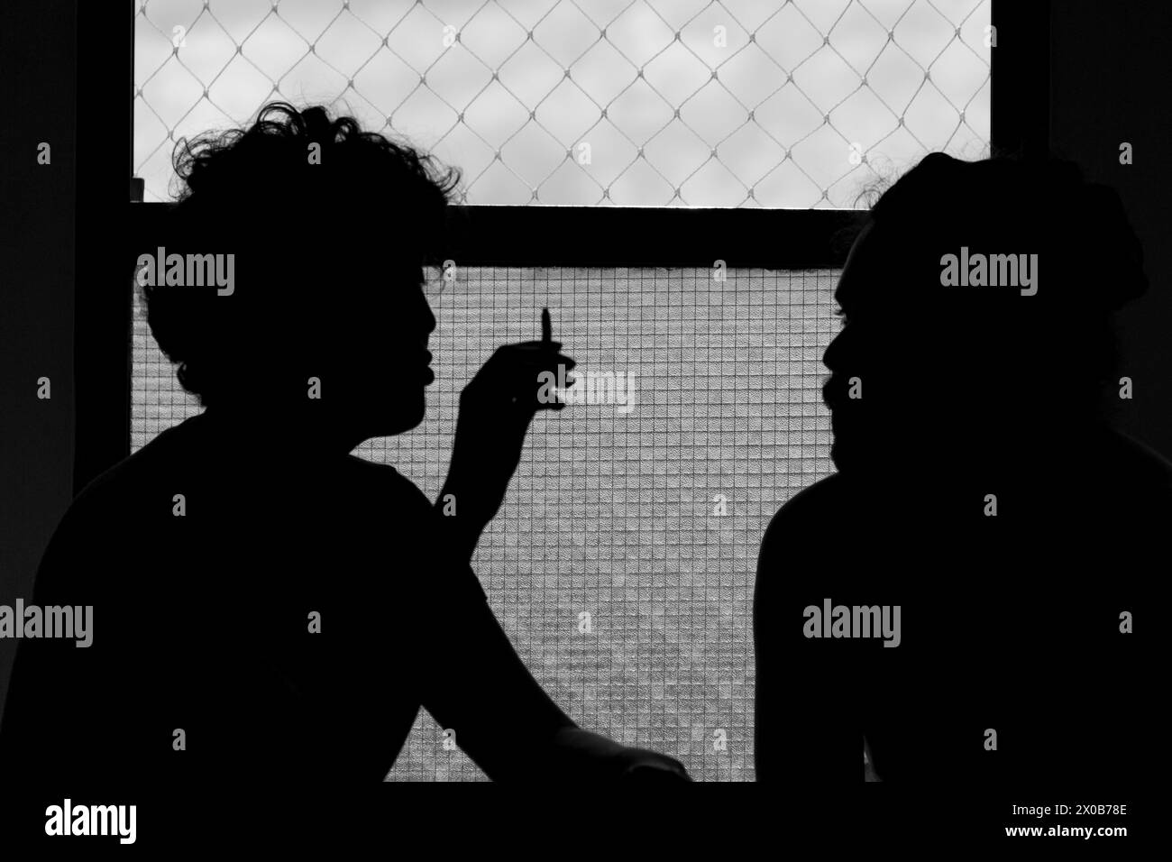 Paare sprechen und rauchen in einer schönen Szene vor dem Fenster in einer schwarz-weißen Silhouette Stockfoto