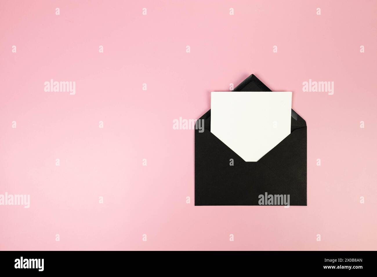 Draufsicht des schwarzen Umschlags, weiße Karte auf rosafarbenem Hintergrund. Pfosten Sie flach. Kopierbereich. Stockfoto