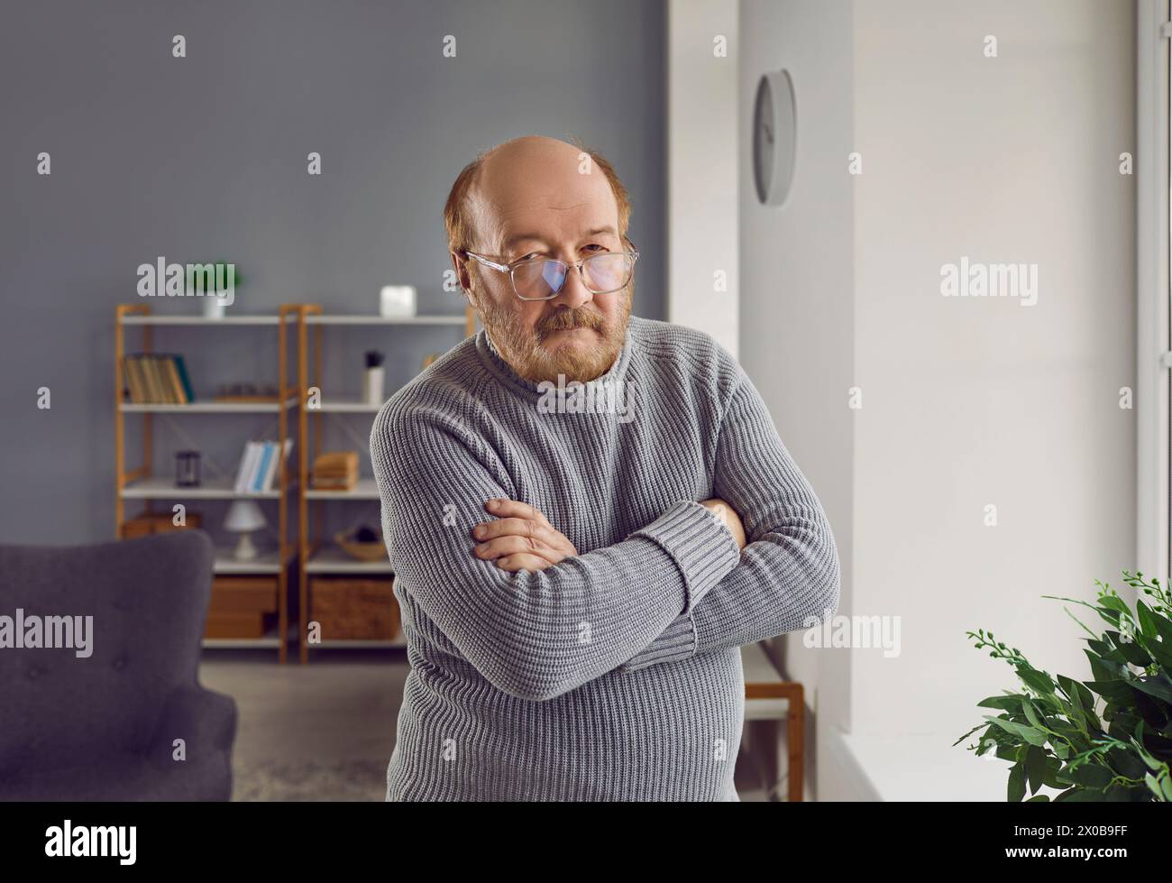 Porträt eines ernsten älteren Mannes, der mit gefalteten Armen steht Stockfoto