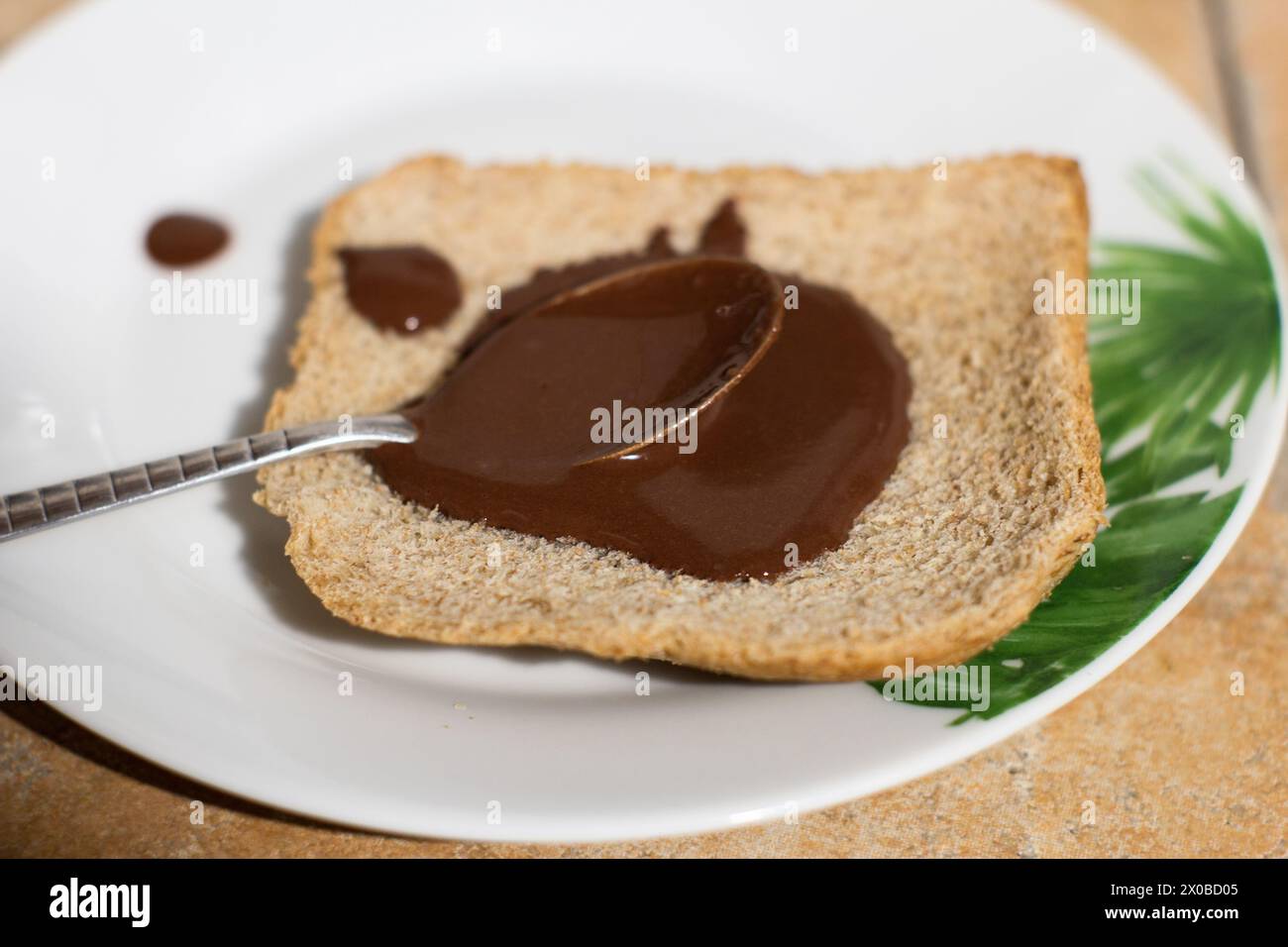 Ein Nahaufnahme-Bild, das den wunderbaren Moment des Verbreitens von reichhaltiger, cremiger Schokolade auf einer frischen Brotscheibe auf einem lebendigen Teller feststellt. H Stockfoto
