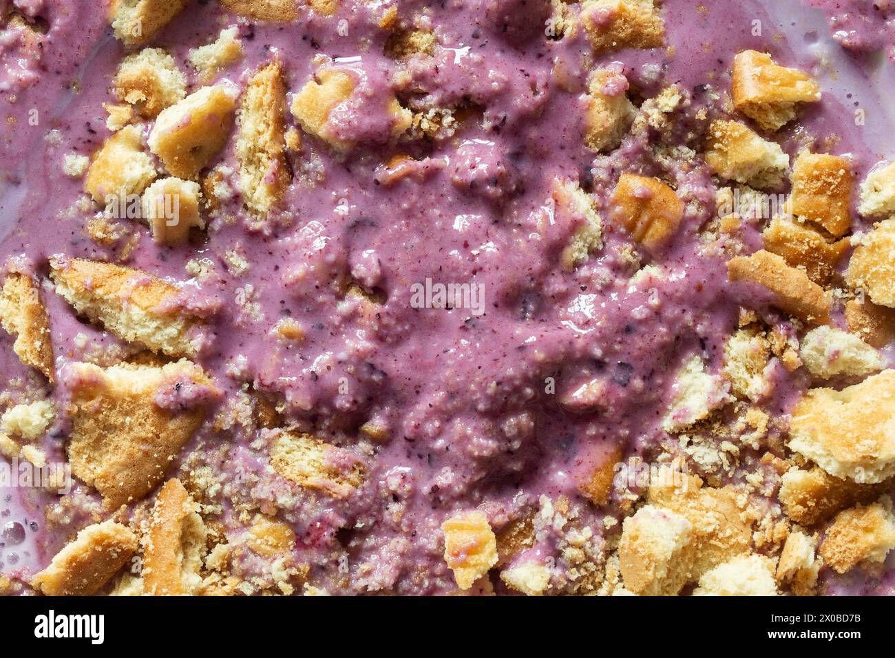 Blick von oben auf eine cremige Textur einer violetten Smoothie-Schüssel mit gemischten Beeren, bestreut mit einer Schicht zerquetschter goldener Kekse, die ein optisches Erscheinungsbild erzeugt Stockfoto