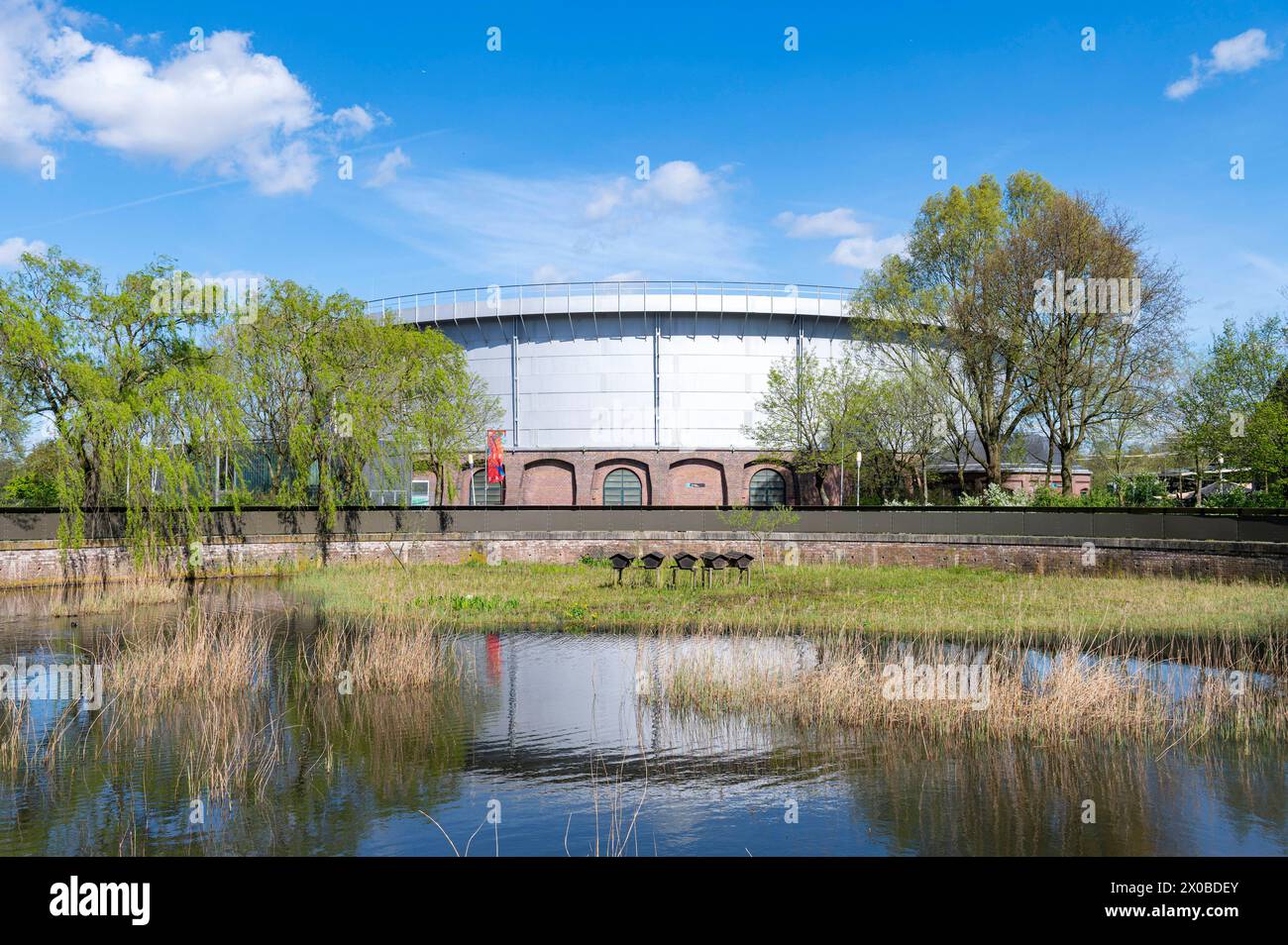 Amsterdam Niederlande 10. April 2024 Gashouder ehemalige Westergasfabriek spiegelte sich an einem blauen Frühlingstag in einem Pool. Die Western Gas Factory wurde im 19. Jahrhundert entwickelt, um Gas aus Kohle für die Stadt zu liefern. Mit der Entdeckung von Erdgas in den nördlichen Niederlanden wurde die Fabrik überflüssig. Heute wird das Gebiet für kulturelle Zwecke genutzt, wobei der Gastank unter anderem als Veranstaltungsort für Festivals genutzt wird. Stockfoto