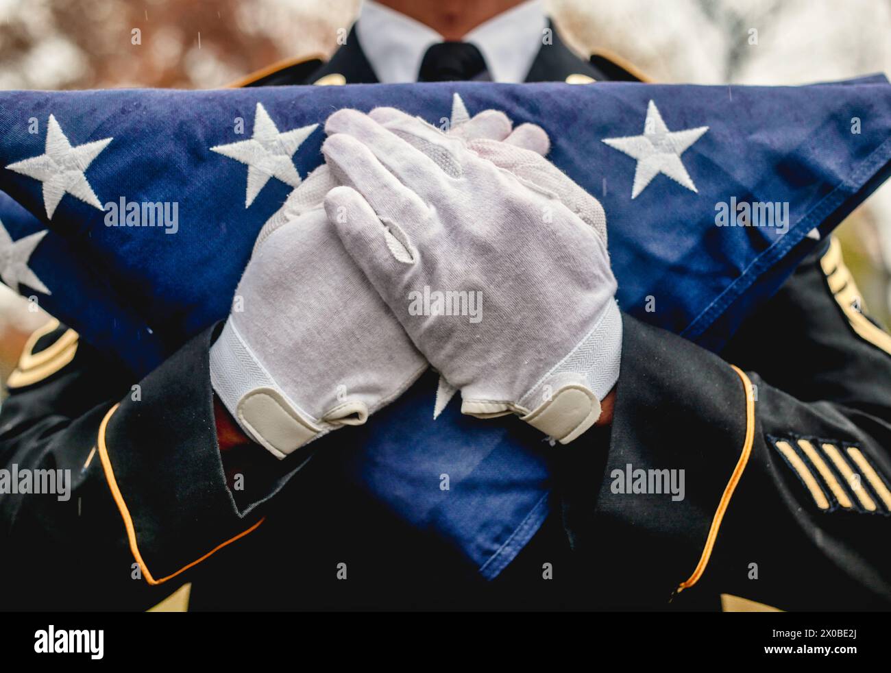 Nahaufnahme eines männlichen Militärsoldaten mit weißen Handschuhen und gefalteter amerikanischer Flagge bei einer Gedenkfeier Stockfoto