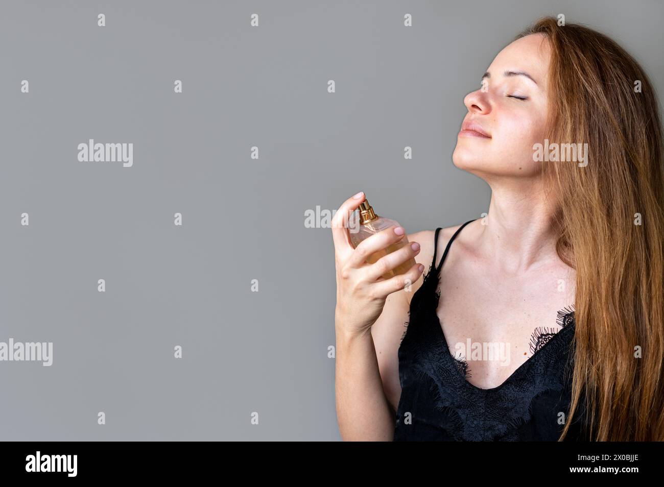 Die Frau sprüht ihr Parfüm auf den Hals und genießt den Duft von Parfüm. Stockfoto