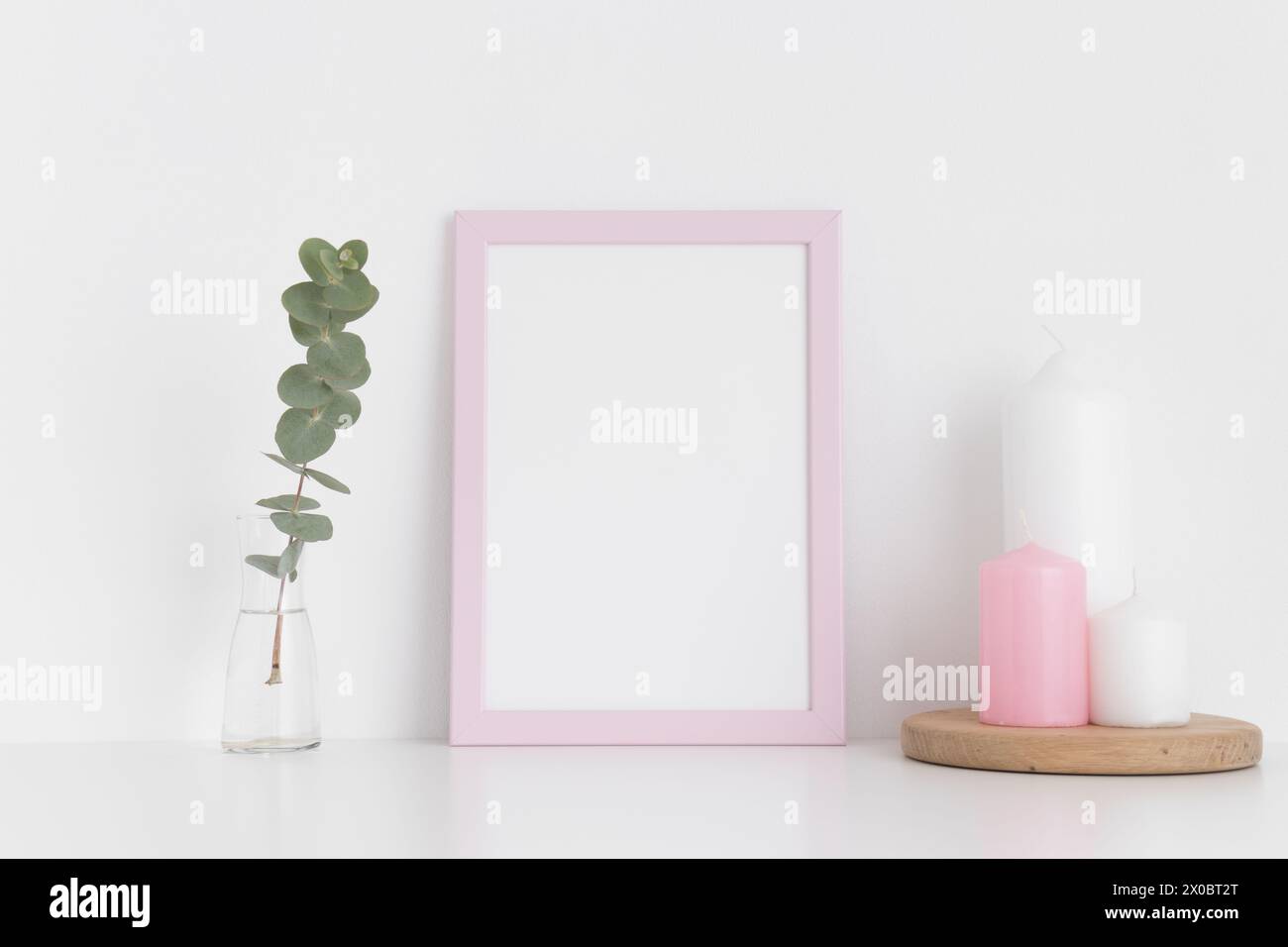 Pinkfarbenes Rahmenmockup mit Kerzen und Eukalyptus in einer Vase auf einem weißen Tisch. Hochformat. Stockfoto