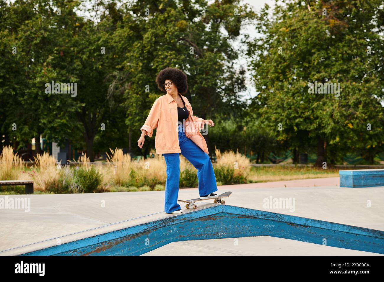 Eine junge Afroamerikanerin mit lockigen Haaren fährt auf einer Rampe in einem Skatepark Skateboard und führt waghalsige Tricks aus. Stockfoto